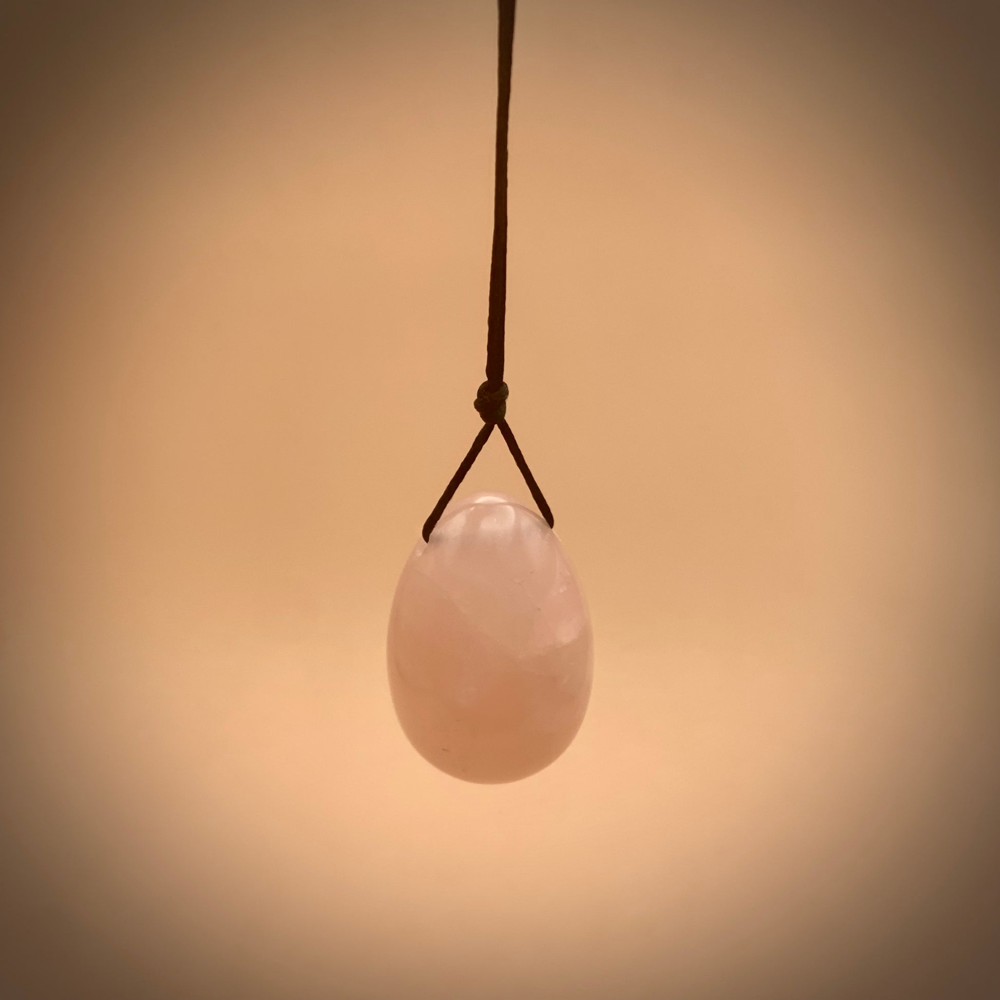 rose quartz crystal egg hanging on satin string