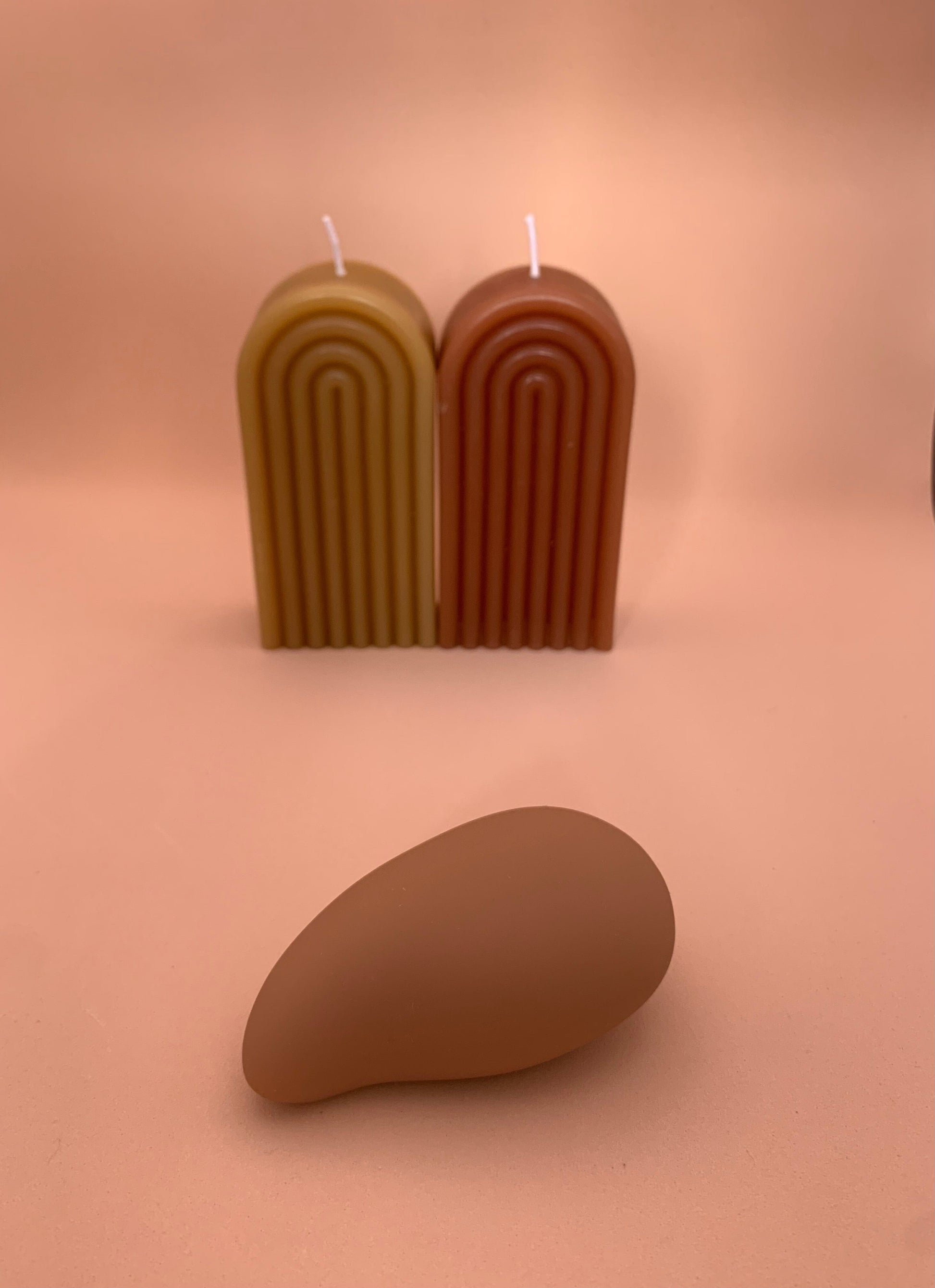 a pebble shaped, nude coloured vibrator in front of two pillar  candles